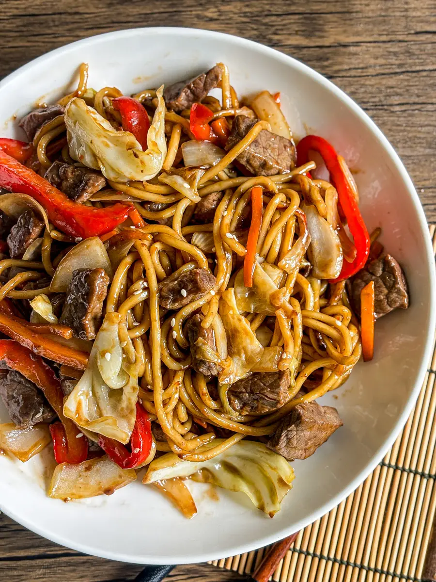 Stir-fried beef yakisoba noodles with cabbage, red bell pepper, and carrots on a white plate.