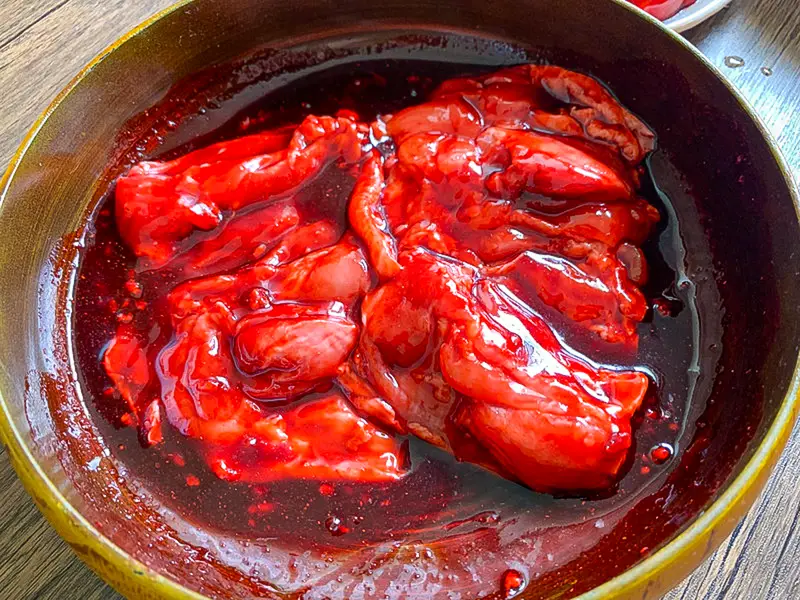 Chicken thighs marinating in glossy red char siu sauce in a ceramic bowl.