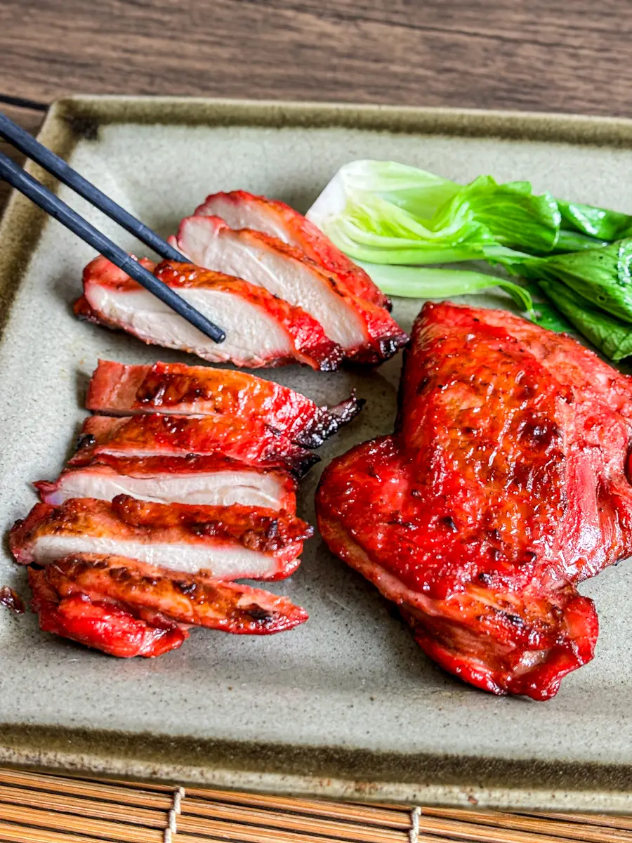 Sliced char siu chicken served with bok choy on a square plate.