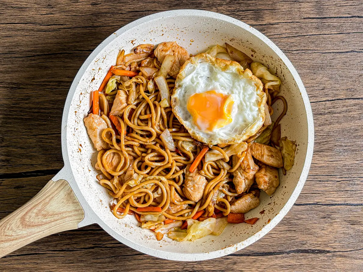Chicken yakisoba noodles cooked in a skillet with glossy sauce and vegetables.