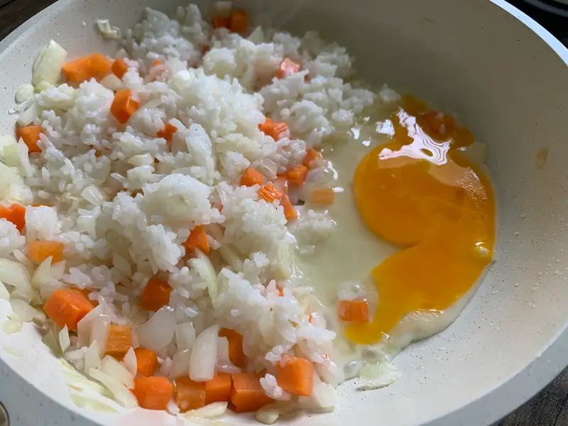 Raw eggs cracked over rice and vegetables, ready to scramble.