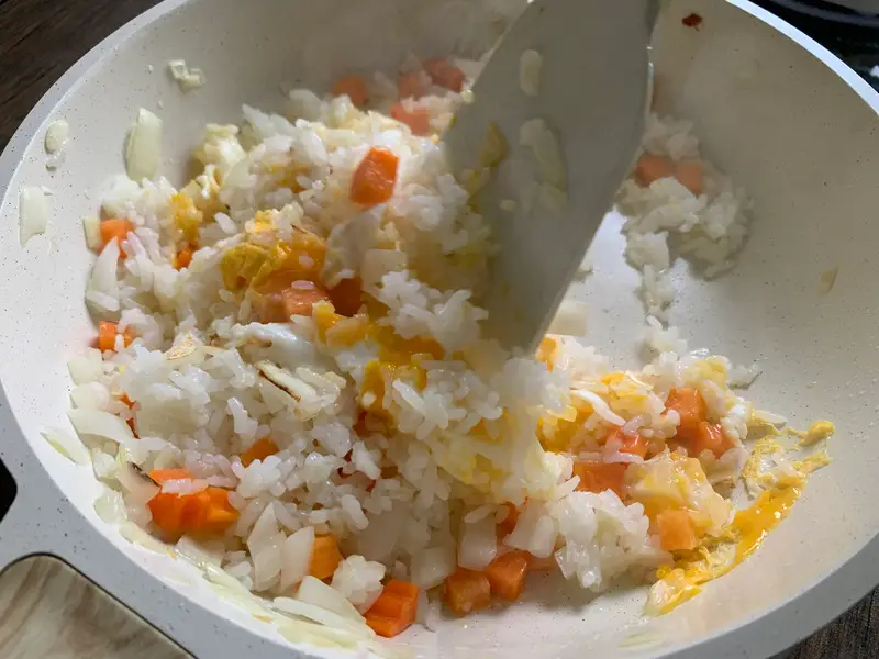 Mixing eggs into hot rice and veggies as they begin to cook.