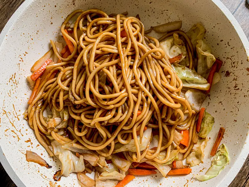 Top-view of yakisoba noodles coated in sauce with vegetable in a white pan.