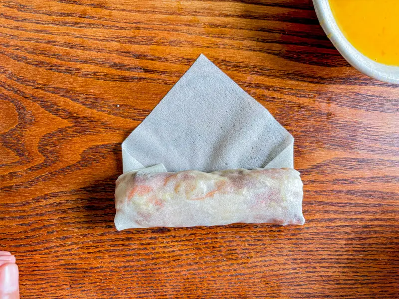 Process of folding a spring roll wrapper on a wooden surface.