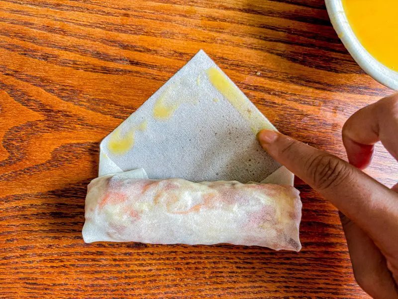 Sealing a spring roll wrapper with egg before finishing the roll.