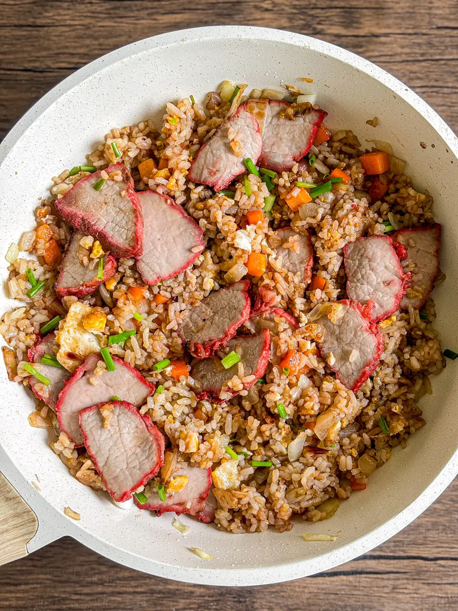 Stir-fried rice with char siu pork in a white pan, showing red-edged pork slices, egg, and diced vegetables.