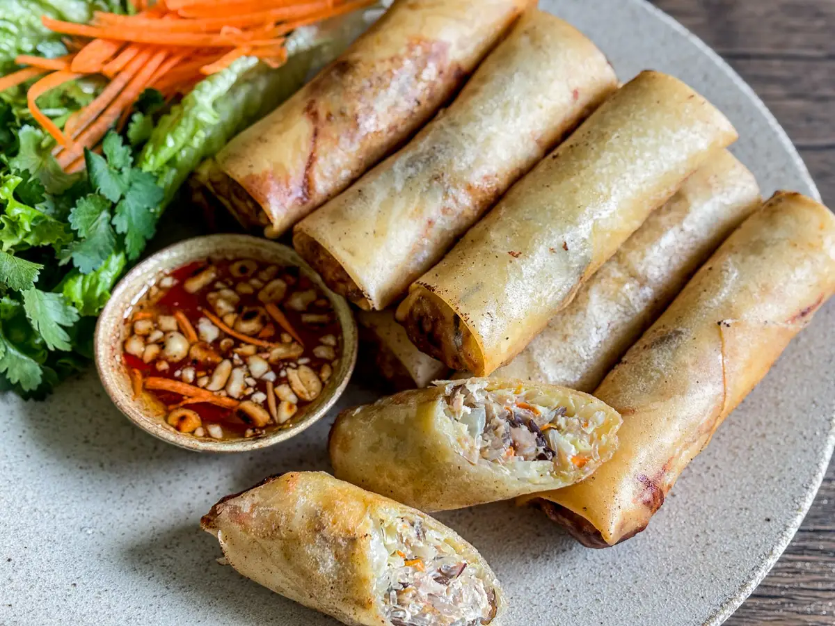 Plate of Lao pork spring rolls served with dipping sauce, fresh herbs, and lettuce.