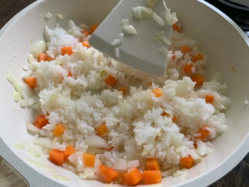 Jasmine rice added to stir-fried vegetables in the pan.