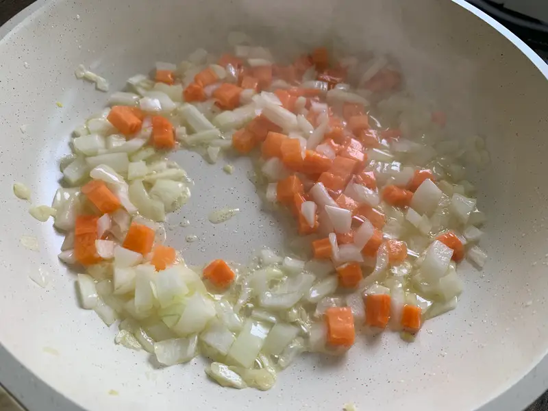 Diced onions and carrots being stir-fried in the pan.