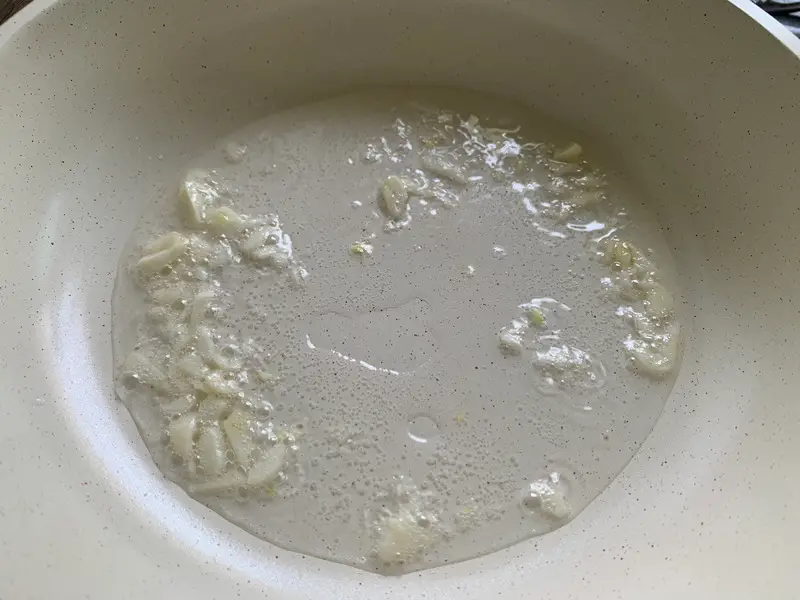 Sautéing minced garlic in oil in a white nonstick pan.