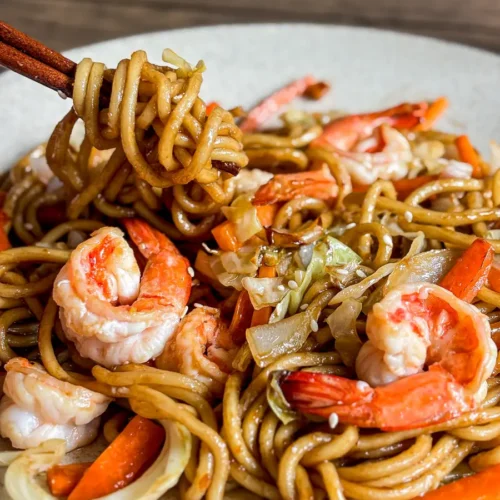 Shrimp yakisoba noodles with cabbage, carrot, and garlic, lifted with chopsticks.