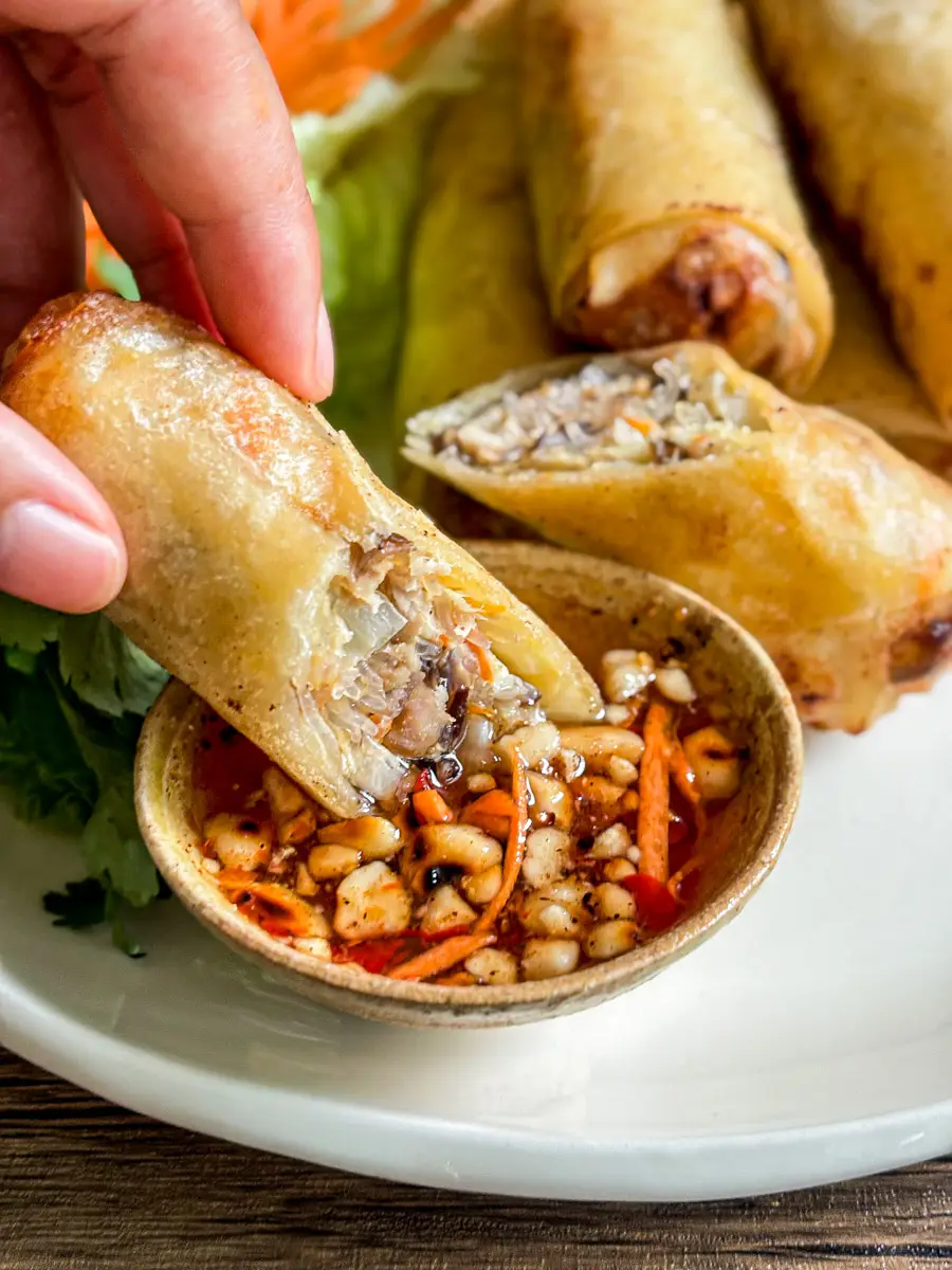 Crispy Lao pork spring roll dipped into a sweet and sour dipping sauce with peanuts and carrot.