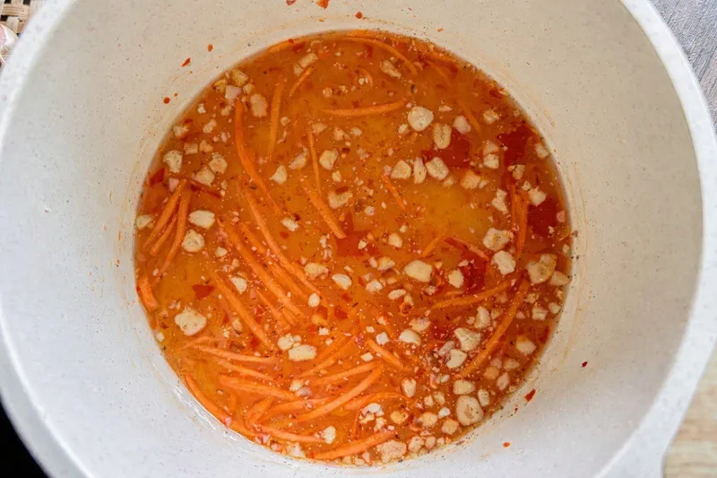 Top-view of Lao spring roll dipping sauce with shredded carrot, chili, and crushed peanuts in a cooking pot.