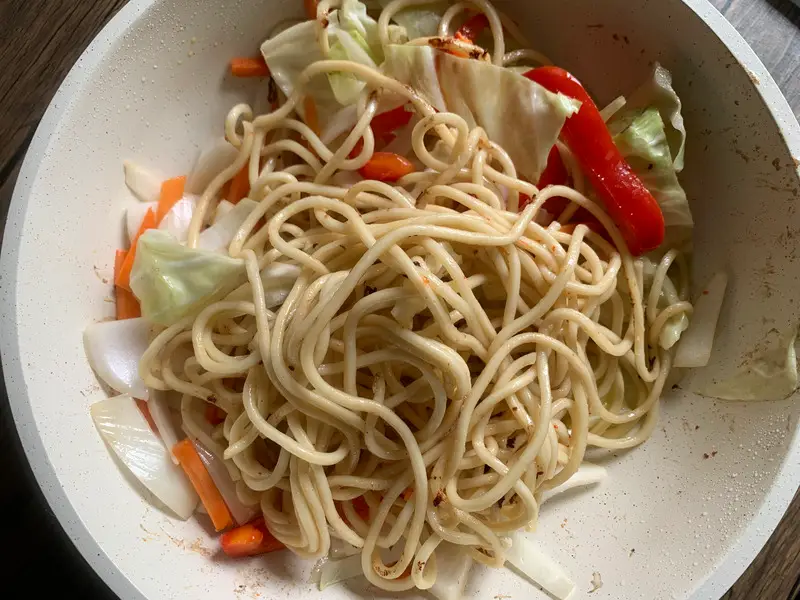 Top-view of yakisoba noodles and sliced vegetables like cabbage, carrots, and bell peppers in a white pan.