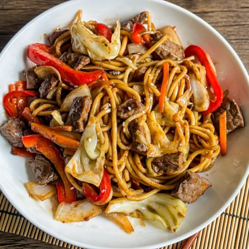 Beef yakisoba noodles stir-fried with vegetables, served on a white dish over wooden table.