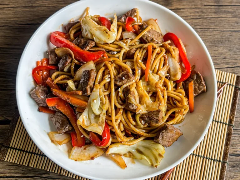 Beef yakisoba noodles stir-fried with vegetables, served on a white dish over wooden table.
