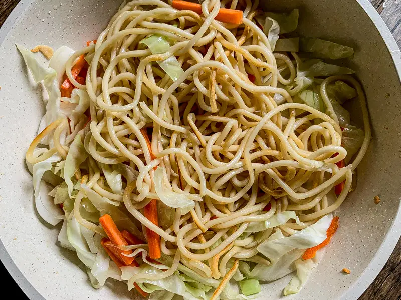 Yakisoba noodles added to sautéed cabbage and carrot in the pan.