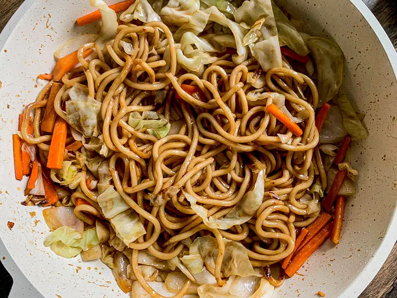 Yakisoba noodles tossed with cabbage, carrot, and sauce in a wide pan.